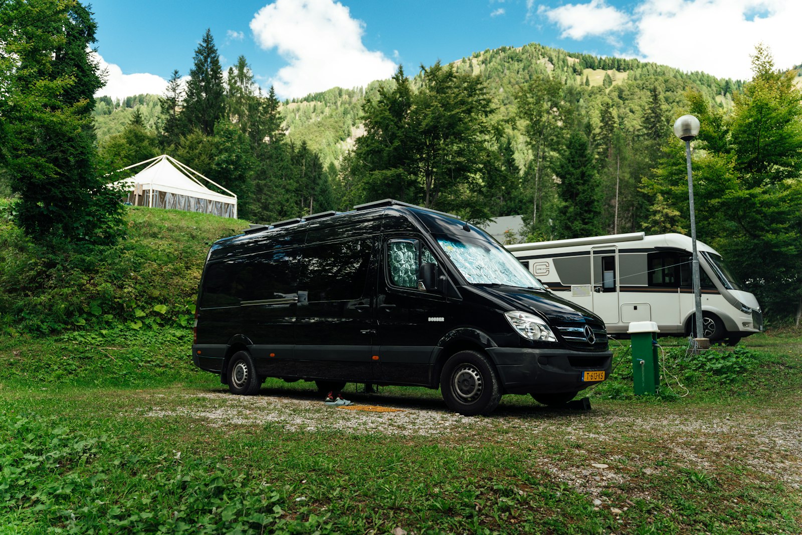Un camper van scuro e un camper con cellula abitativa parcheggiati in un campeggio di montagna